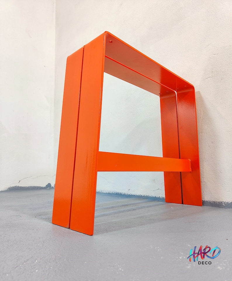 May include: A pair of orange metal A-frame stools. The stools are made of thick metal and have a simple, modern design.