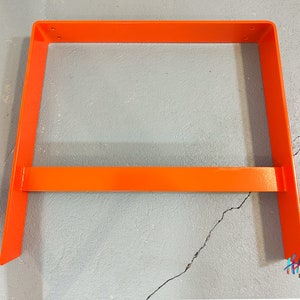 May include: Orange metal frame for a shelf or table. The frame is made of thick metal and has a simple, modern design.