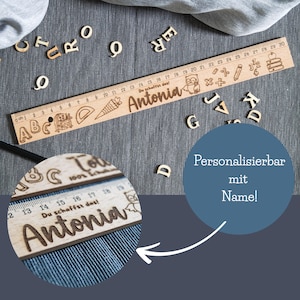 May include: A wooden ruler with a personalized name, "Antonia", engraved on it. The ruler features a colorful design with letters, numbers, and illustrations of school supplies. The text "Du schaffst das!" (You can do it!) is also engraved on the ruler.