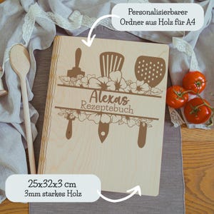Könnte beinhalten: Ein helles Kochbuch aus Holz mit dem Namen "Alexas Rezeptebuch" auf dem Einband. Der Einband zeigt Küchenutensilien-Illustrationen und Blumendesigns. Das Buch misst 25x32x3 cm.