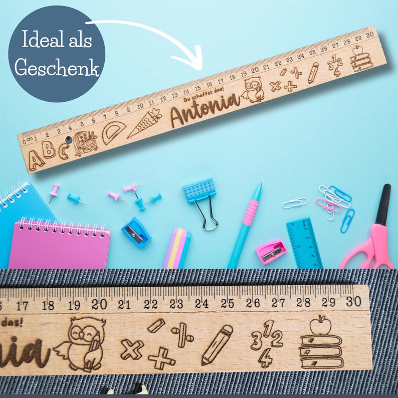 May include: A wooden ruler with a personalized name "Antonia" and the text "Du schaffst das!"  The ruler is decorated with a cartoon owl, a pencil, a carrot, a stack of books, and math symbols. The ruler is 30 cm long.