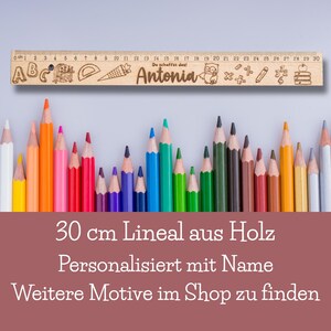 May include: A wooden ruler with a personalized name "Antonia" and a variety of school-themed illustrations, including letters, numbers, a pencil, a ruler, a carrot, an owl, and a stack of books. The ruler is 30 inches long and is surrounded by a row of colored pencils.