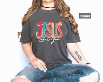 May include: A dark gray t-shirt with the text "JESUS Loves You" in colorful, stylized lettering. The shirt is a comfortable, casual style, perfect for everyday wear.