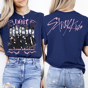 K&ouml;nnte beinhalten: Marineblaues T-Shirt mit einem rosa Aufdruck, der eine Gruppe von Personen, das Wort "doit" und den Text "SKZ IT TAPE STRAY KIDS" zeigt. Auf der R&uuml;ckseite des Shirts steht der Text "Stray Kids" in Rosa. Das Shirt ist aus weichem Material.