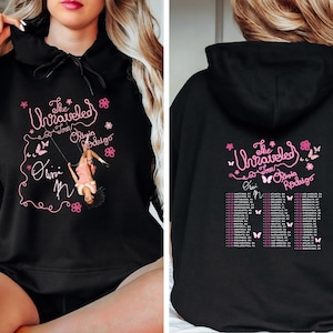 May include: A black hooded sweatshirt featuring a pink graphic on the front with the text The Unraveled Tour Olivia Rodrigo and an illustration of a person on a swing. The back displays the same text with a list of tour cities and dates.