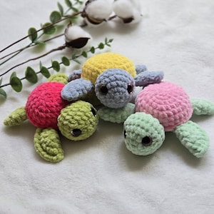 Puede incluir: Tres juguetes de tortuga de crochet en diferentes colores: verde, rosa y amarillo. Las tortugas tienen ojos negros y están hechas con un hilo suave y peludo.