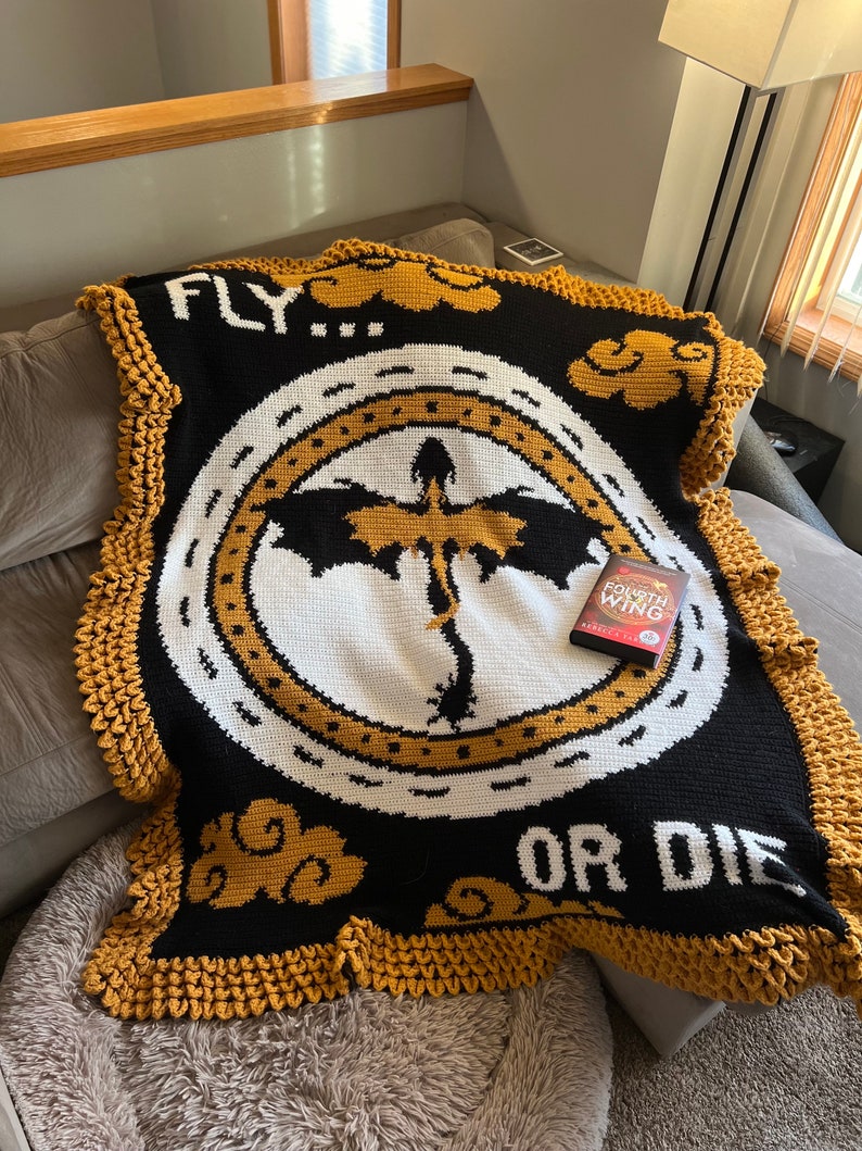 K&ouml;nnte beinhalten: Eine schwarz-wei&szlig;e H&auml;keldecke mit gelbem Rand. Die Decke zeigt einen Drachen in einem Kreis mit den Worten "FLY... OR DIE" und einem Wolkenmuster. Ein DVD-Geh&auml;use f&uuml;r den Film "Drachenz&auml;hmen leicht gemacht" liegt auf der Decke.