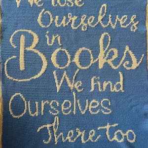 May include: A blue crocheted blanket with the text "We lose ourselves in books. We find ourselves there too." in yellow yarn.