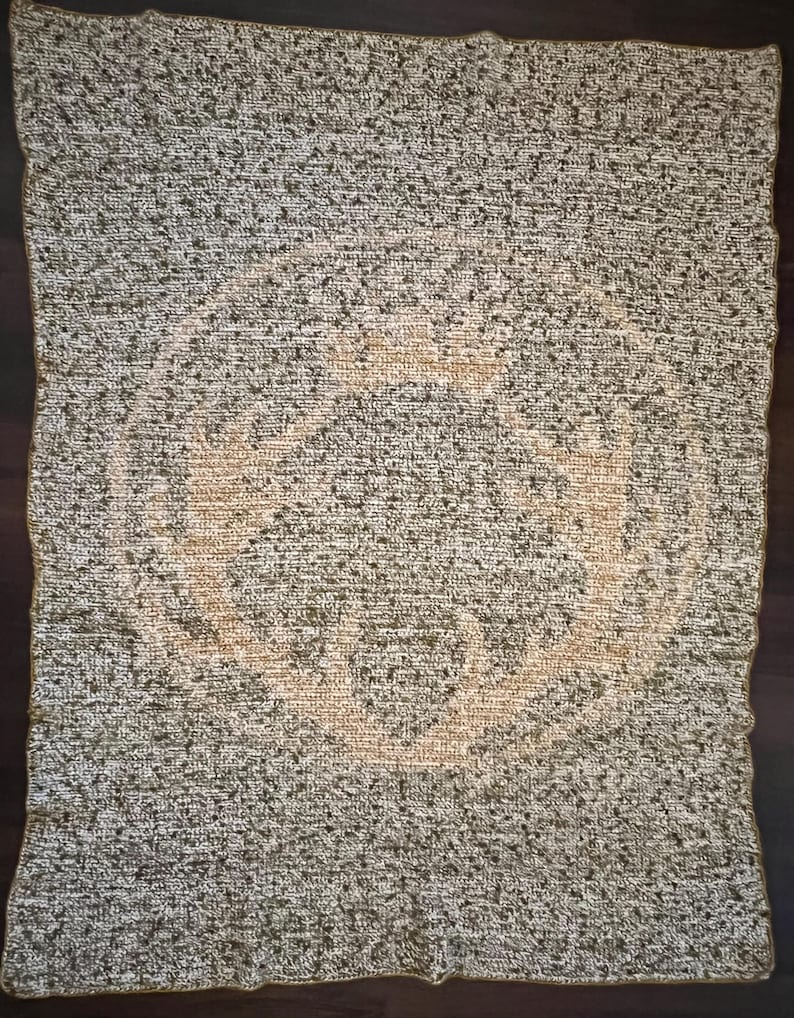 Op de afbeelding: Een bruin en wit gebreid deken met een groot, beige, cirkelvormig ontwerp in het midden.
