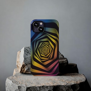 May include: A smartphone case with a colourful, geometric design. The case features a repeating, spiralling pattern in shades of blue, yellow, and pink. The phone case is resting on a rough, grey stone surface.