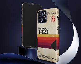 Może przedstawiać: Etui na telefon w stylu vintage z retro wzorem kasety VHS. Etui ma czarne tło z wyblakłym, żółtawym wzorem kasety VHS. Etykieta kasety zawiera napis "Dynamicron T-120" i "Seven Samurai". Etui jest zaprojektowane do telefonu iPhone.