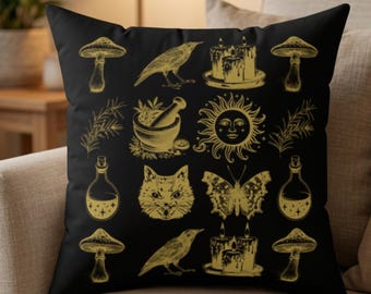 May include: A black square throw pillow featuring a repeating gold-colored print of various icons including mushrooms, birds, candles, a mortar and pestle, a sun with a face, a cat head, a butterfly, and glass bottles with liquid and stars.