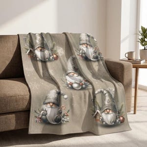 May include: A beige throw blanket featuring a repeating pattern of gnomes wearing textured grey hats. The gnomes are surrounded by white snowflakes, small pine branches, candy canes, and gift boxes, creating a festive winter-themed design.