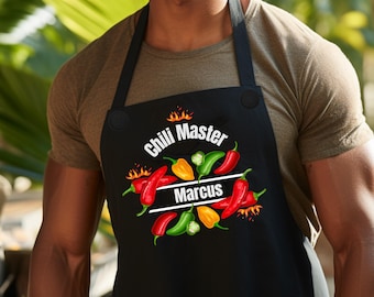 May include: Black apron with the text "Chili Master" and the name "Marcus" in white. The apron features a colorful design of chili peppers in red, green, and yellow, with flames. The apron is worn by a person.