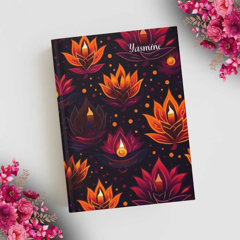 A journal with a floral design on it on a table with pink flowers around it