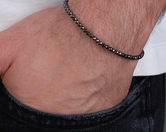 Pode incluir: Um bracelete preto de contas com um brilho sutil. O bracelete é usado no pulso.