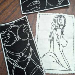 Könnte beinhalten: Drei gestickte Aufnäher mit schwarz-weißen Designs. Einer zeigt eine Frauenfigur in einer Strichzeichnung. Ein anderer zeigt ein Dessous-Design. Der dritte zeigt Hände und ein Piercing.