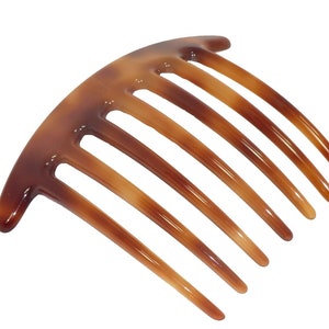 May include: A brown hair comb with seven curved teeth. The comb has a curved top and is made of a glossy, translucent material. The color transitions from a darker brown at the top to a lighter brown at the teeth.