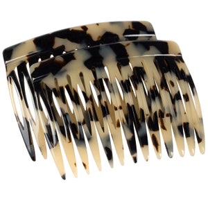 May include: Two tortoiseshell hair combs with a curved shape and a row of teeth. The combs are made of a brown and white mottled plastic.