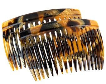 Puede incluir: Dos peines para el cabello de carey con un patrón negro y marrón. Los peines son curvos y tienen una fila de dientes en un lado.