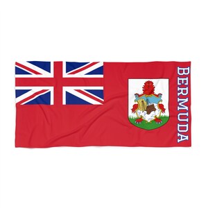 May include: A red beach towel featuring the flag of Bermuda. The flag displays a red and blue Union Jack in the top left corner and the Bermuda coat of arms on the right. The word "BERMUDA" is written vertically in blue on the right side of the towel.