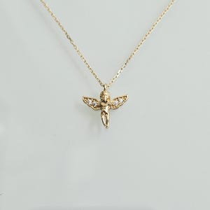 May include: A gold chain necklace with a small cherub pendant adorned with tiny clear stones.
