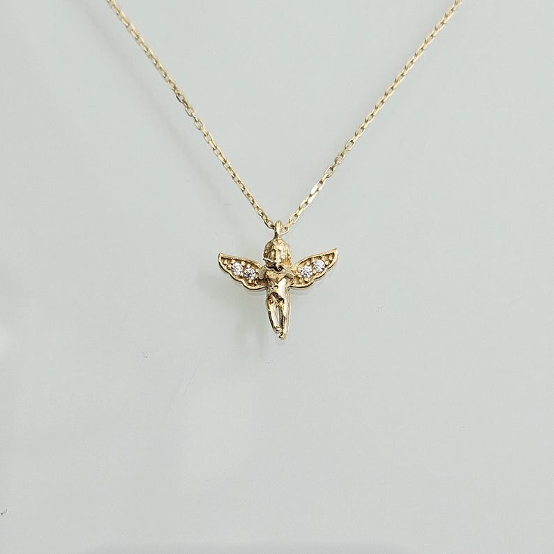 May include: A gold chain necklace with a small cherub pendant adorned with tiny clear stones.
