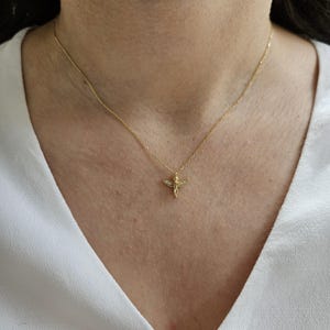 May include: A gold chain necklace with a small angel pendant featuring clear cubic zirconia stones.