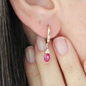 May include: Gold hoop earrings with a dangling pink oval gemstone and small clear gemstones.