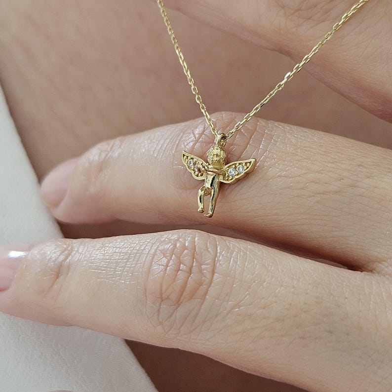 May include: A gold necklace with a small cherub pendant adorned with tiny clear stones.