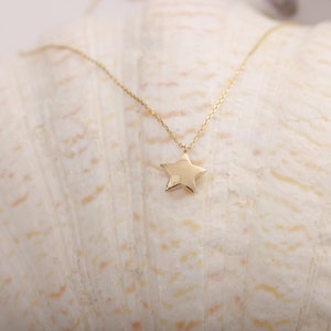 May include: A gold star pendant necklace on a white seashell background.