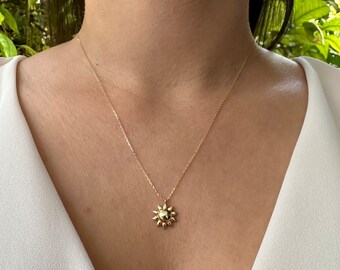 May include: A gold necklace with a sun pendant. The pendant is a stylized sun with a round center and rays extending out.