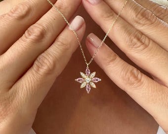 May include: A gold chain necklace with a pink and white flower pendant. The flower pendant has a center stone surrounded by smaller stones.
