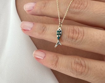 May include: A gold chain necklace with a small blue and white fish pendant. The fish has a detailed design and a small evil eye charm.
