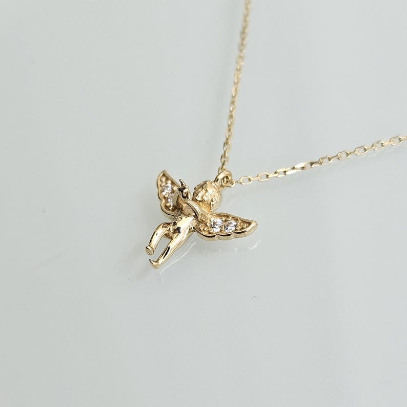 May include: A gold necklace with a small cherub pendant adorned with clear cubic zirconia stones.