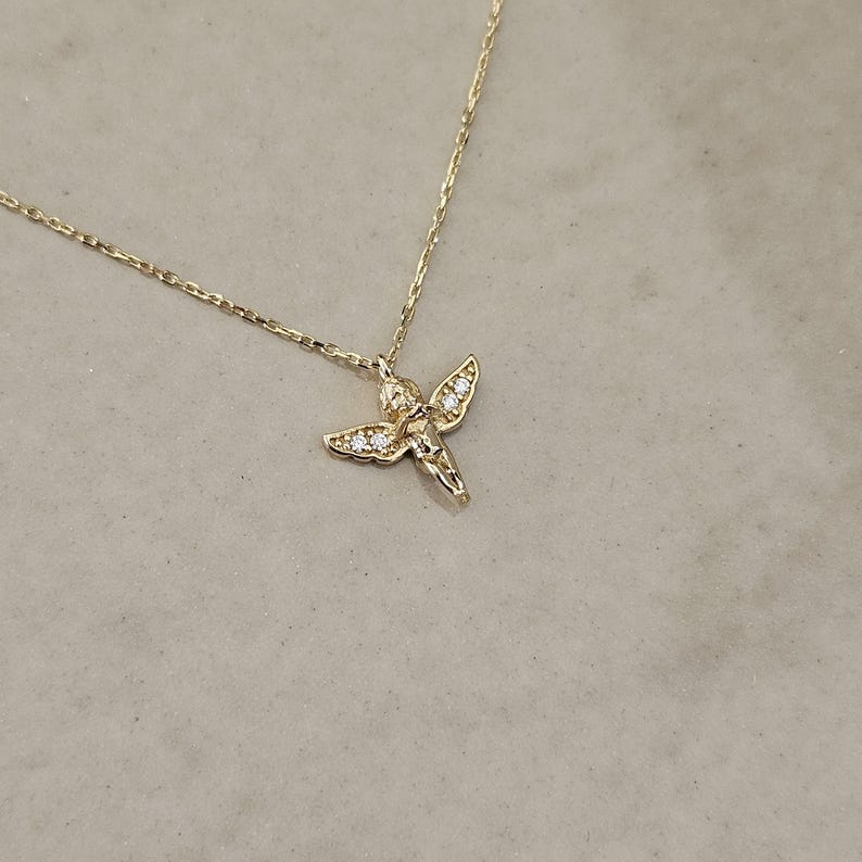 May include: A gold chain necklace with a small, detailed angel pendant adorned with tiny clear cubic zirconia stones.