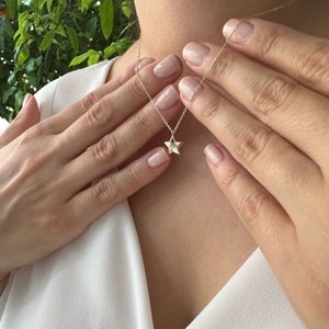 May include: A gold chain necklace with a small, star-shaped pendant. The pendant has a clear stone in the centre.