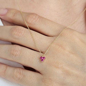 May include: A delicate gold chain necklace with a small pendant featuring three pink gemstones.