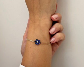 May include: A gold chain bracelet with a blue sapphire flower charm. The flower charm has a small diamond in the center.