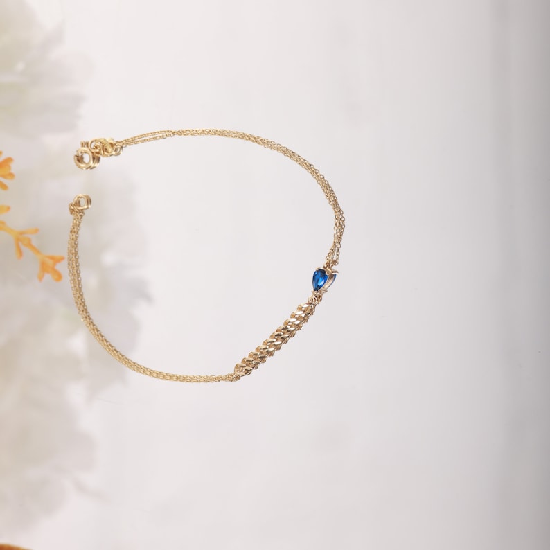 A tiny fine chain bracelet with a raindrop sapphire gemtstone and a piece of gourmet chain in the center. Birthstone for september.