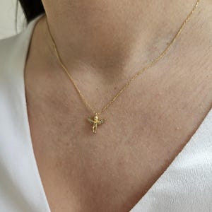 May include: A gold chain necklace with a small, detailed angel pendant. The angel has wings and is adorned with tiny clear stones.