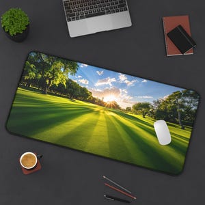 Peut inclure: Tapis de bureau rectangulaire avec une scène de parcours de golf au coucher du soleil. Le tapis a une bordure noire et une souris d'ordinateur blanche est sur le côté droit. Un ordinateur portable, une tasse à café et un carnet sont également sur la surface sombre.