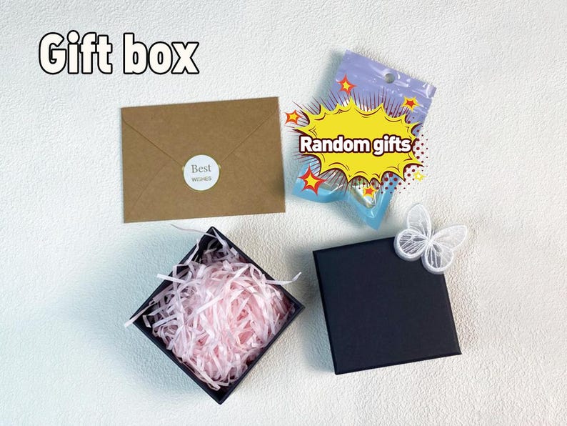 May include: A black gift box with pink tissue paper inside. A brown envelope with the text "Best Wishes" is in the background. A small plastic bag with the text "Random gifts" is also in the background.