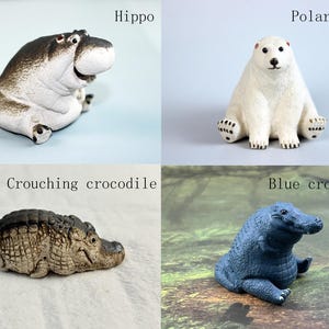 May include: Four ceramic animal figurines: a hippopotamus, a polar bear, a crouching crocodile, and a blue crocodile. The hippopotamus is brown and white, the polar bear is white, the crouching crocodile is brown and green, and the blue crocodile is blue.