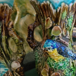 Puede incluir: Dos jarrones de cerámica con un diseño de corteza de árbol texturizada en tonos marrones y verdes. Cada jarrón tiene un borde interior de color turquesa brillante y un pájaro esculpido con plumaje azul, amarillo y negro posado entre hongos.