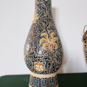 Peut inclure: Un grand vase en céramique en forme de poire avec un fond bleu sarcelle foncé orné d'un motif répétitif complexe de fleurs et de feuillages tourbillonnants dans des tons crème et jaune doré. La base est crème avec une bordure géométrique.