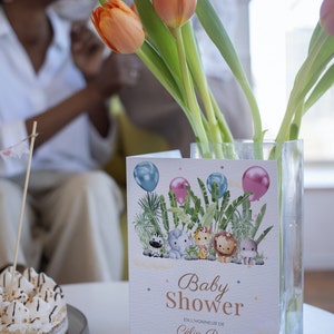 Pu&ograve; includere: Un invito a un baby shower a tema giungla. L'invito presenta una zebra, un elefante, un leone e un ippopotamo. Il testo sull'invito recita "Baby Shower" e "C&eacute;lia Boro". L'invito include anche la data, l'ora e la posizione del baby shower.