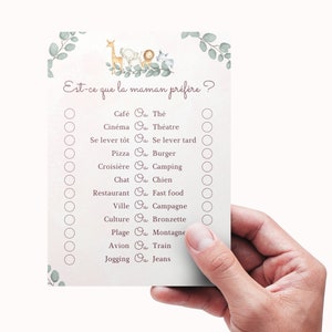 May include: A pink and white baby shower game card with the text "Est-ce que la maman pr&eacute;f&egrave;re?" and a list of questions with two options each. The options are separated by the word "Ou". The card features a cartoon illustration of a giraffe, elephant, lion, and monkey.