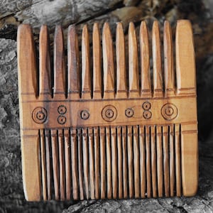 Puede incluir: Un peine de madera con un diseño decorativo de círculos. El peine es de color marrón y está hecho de madera. El peine está sobre una superficie de madera.