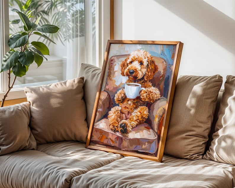 May include: A framed artwork showing a brown Goldendoodle dog in a chair, holding a white coffee cup. The dog is the central figure, with a soft, fluffy appearance. The artwork is set against a neutral background, with a wooden frame.